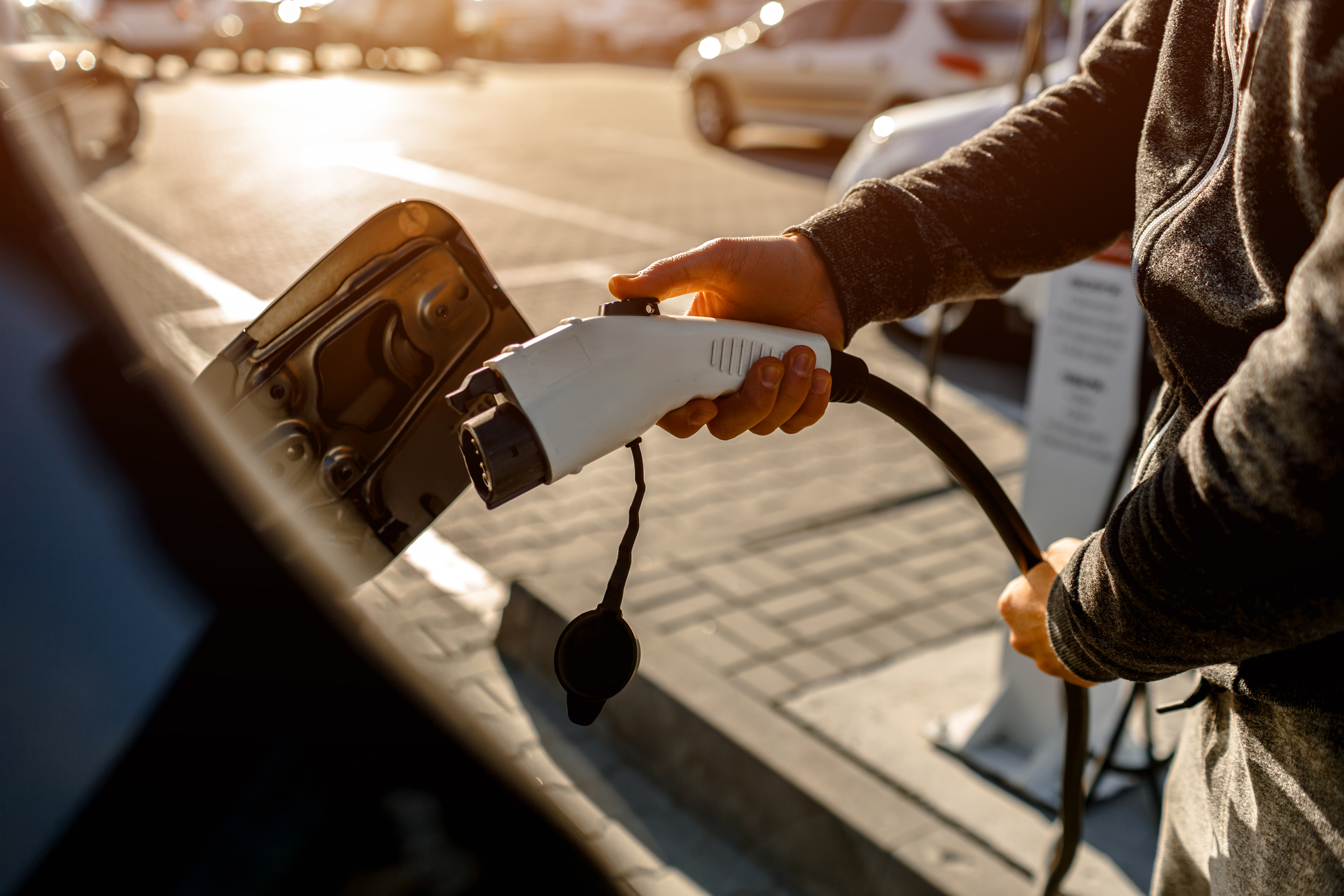 açık otoparkta elektrikli araba için güç şarj kablosunu tutan adam