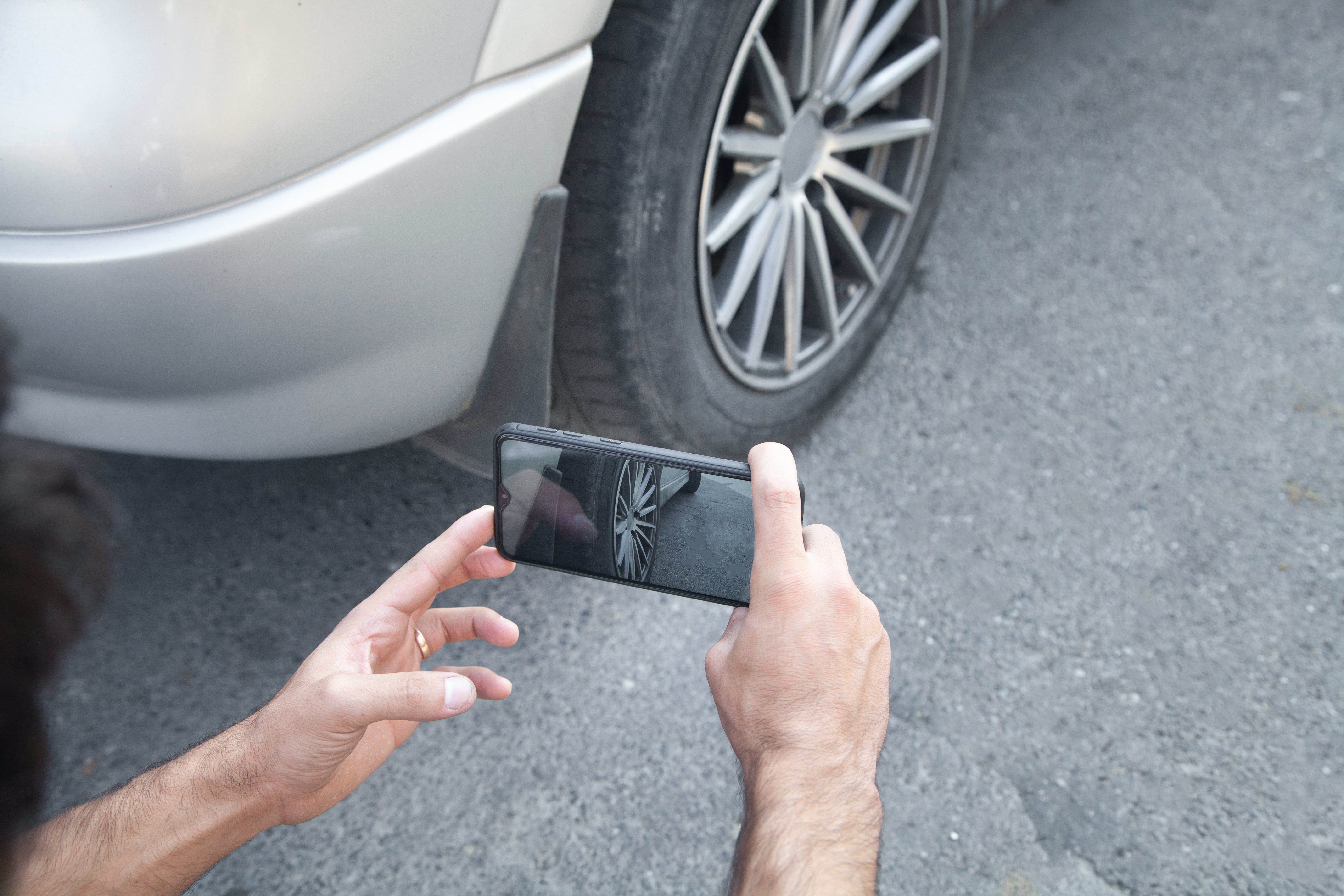 Telefonuyla bir araba tekerleğinin fotoğrafını çeken kişi